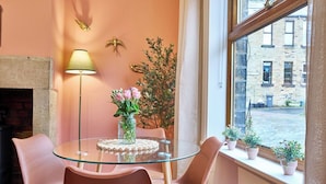 A room with a glass table, pink chairs, a vase with flowers, a lamp, and a view of buildings through a window. - Stylish 2BR Home | Central Hebden Bridge Escape (Hebden Bridge)