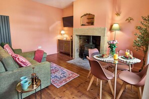 Ein gemütliches Wohnzimmer mit Sofa, Couchtisch, Kamin und Essbereich mit Stühlen und einem für das Frühstück gedeckten Tisch.