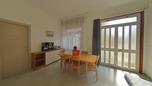 Un coin repas avec une table et des chaises, un téléviseur posé sur un meuble, un four à micro-ondes et une fenêtre avec des rideaux.