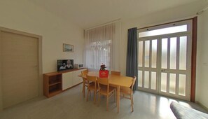 Ein Essbereich mit Tisch und Stühlen, einem Fernseher auf einem Schrank, einer Mikrowelle und einem Fenster mit Vorhängen.