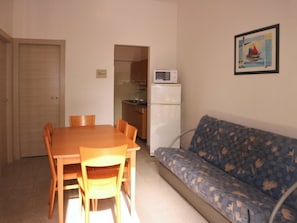 Ett kompakt bostadsutrymme med ett matbord, stolar, en soffa, ett litet kök med mikrovågsugn och en dörr.