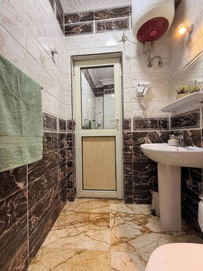 A bathroom with a marble floor, a sink, a mirror, a towel, and a shower area. - Charming 2-bedroom Apartment in the Heart of Hurghada (Hurghada)
