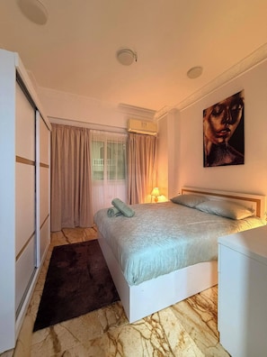 A bedroom with a bed, a bedside lamp, a painting on the wall, and a window with curtains. - Charming 2-bedroom Apartment in the Heart of Hurghada (Hurghada)