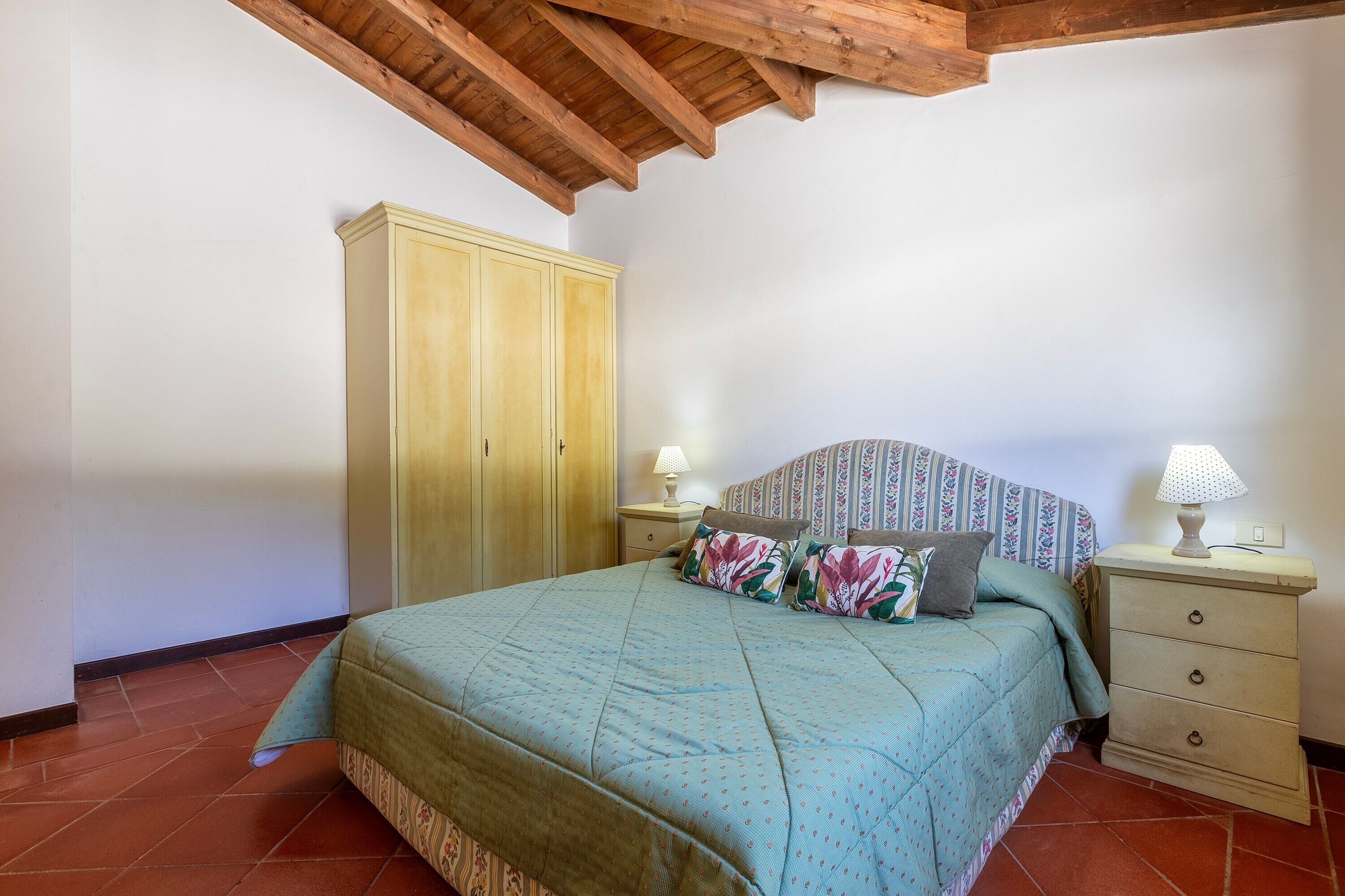 A bedroom with a bed, nightstands, a wardrobe, and a wooden ceiling.