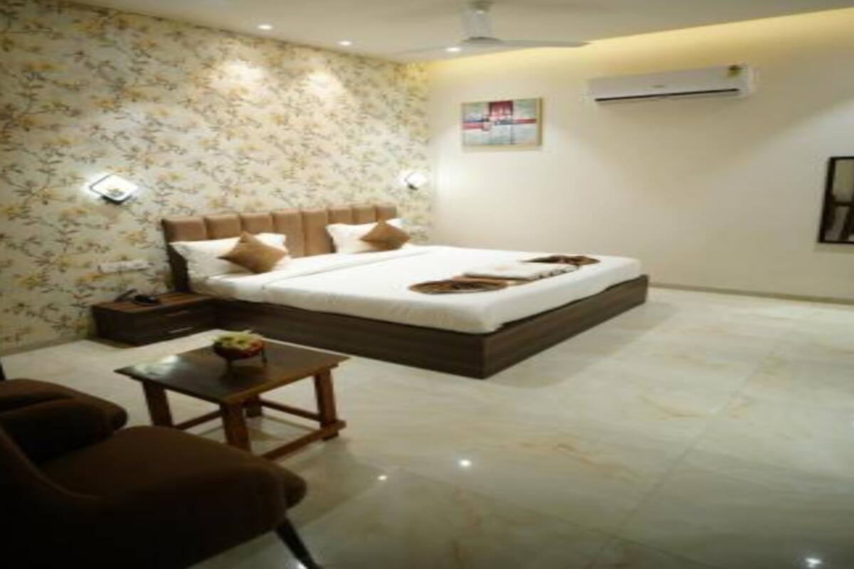 A bedroom with a bed, nightstands, a chair, a small table, and an air conditioning unit.