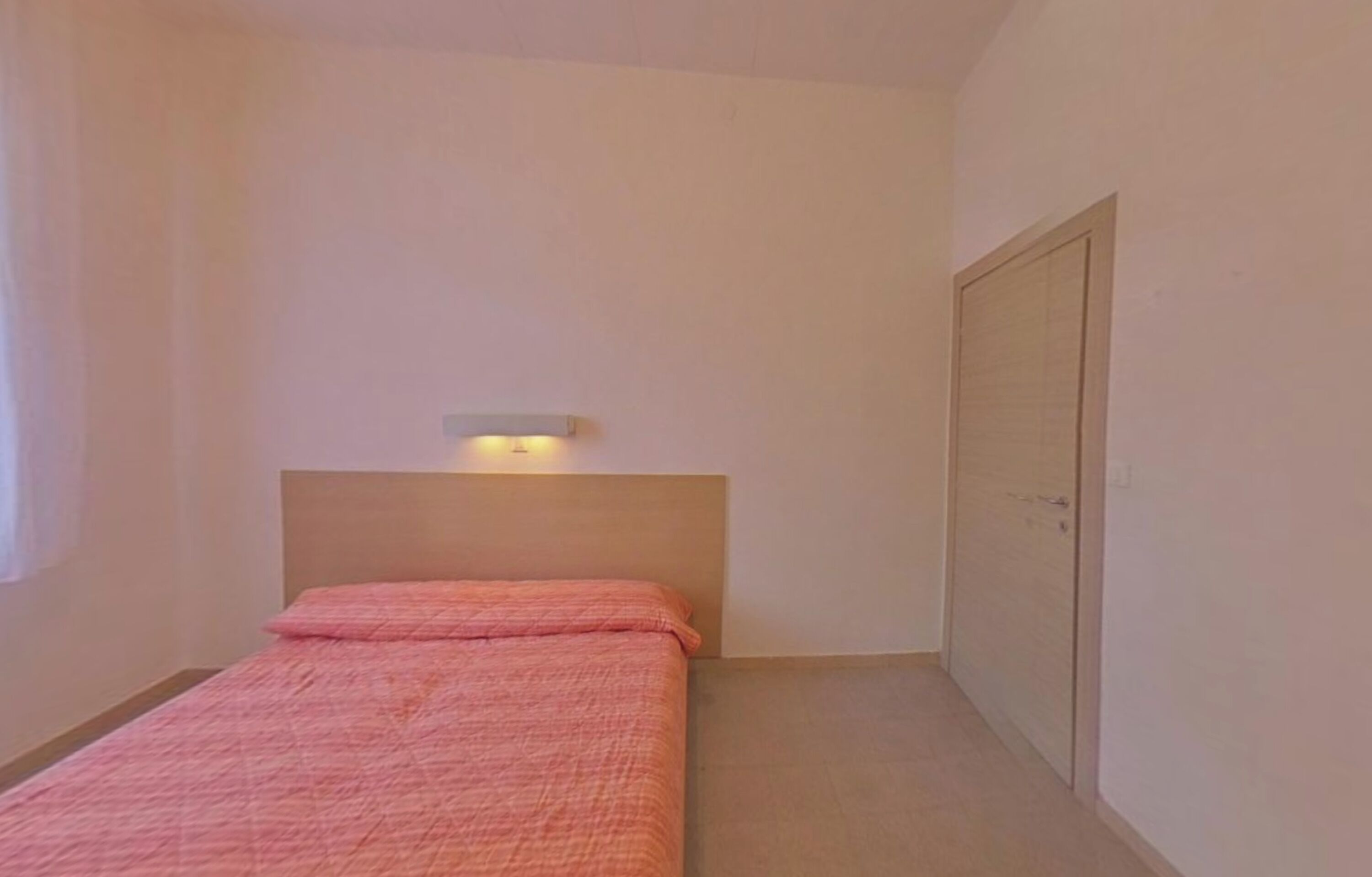 A small, single-bed room with a plain headboard, a bedside table, and a door.