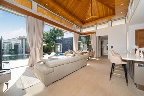 A spacious living area with a large sofa, a dining table, and a kitchen area. - New Luxury 4BR Pool Villa: Elite Luxury D06 (Tambon Thep Krasatti)