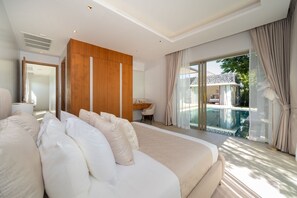 A modern bedroom with a large bed, a wooden panel wall, a desk, and a view of a swimming pool. - New Luxury 4BR Pool Villa: Elite Luxury D06 (Tambon Thep Krasatti)