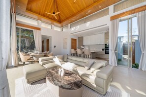 A spacious living area with a large sectional sofa, a marble coffee table, and a modern kitchen in the background. - New Luxury 4BR Pool Villa: Elite Luxury D06 (Tambon Thep Krasatti)