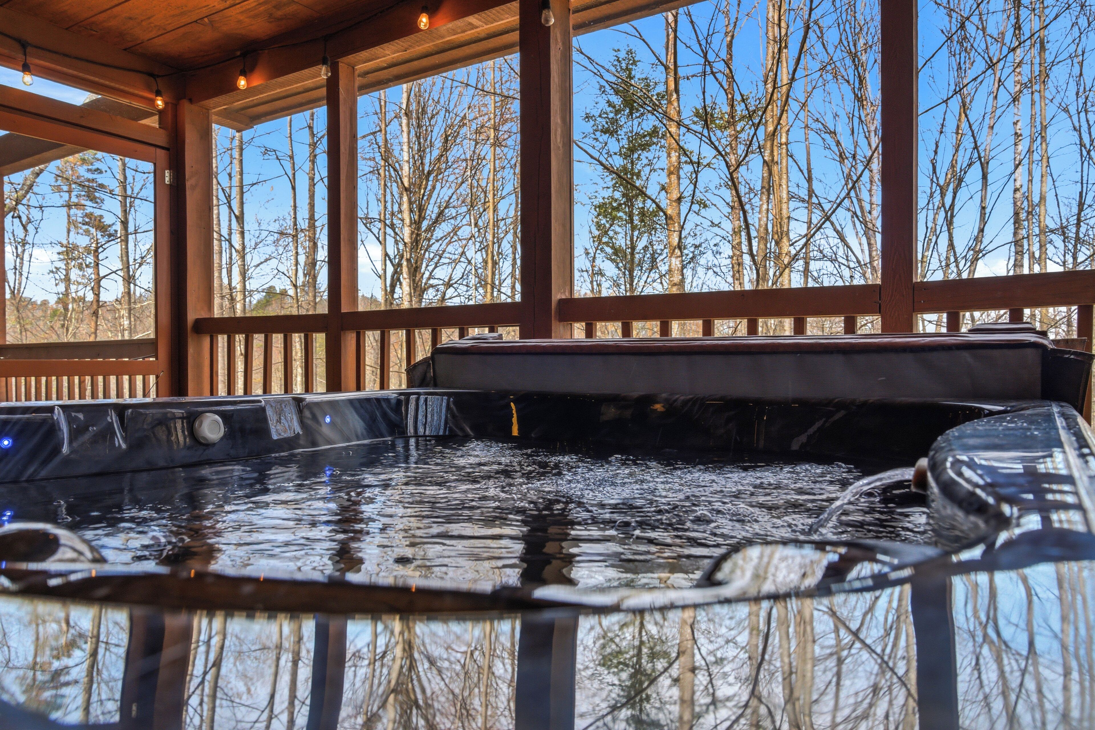 A hot tub with a wooden deck and large windows overlooking a forest.