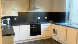Een compacte keuken met een magnetron, oven, wasmachine en een hanglamp.