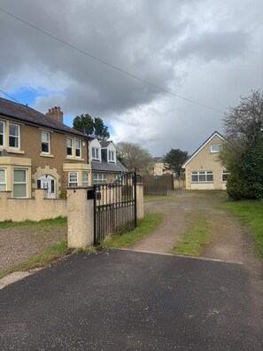 Una strada residenziale con case, un vialetto recintato e cielo sereno.