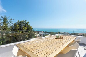 Ein Holztisch mit Stühlen auf einem Balkon mit Blick auf eine Küstenstadt.