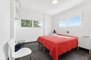 Ein Schlafzimmer mit einem Bett, einem Schreibtisch, einem Stuhl und zwei Fenstern.