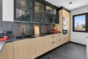 Eine moderne Küche mit schwarzer Arbeitsplatte, Holzschränken und einem Glaskasten-Oberschrank, der Gläser präsentiert.