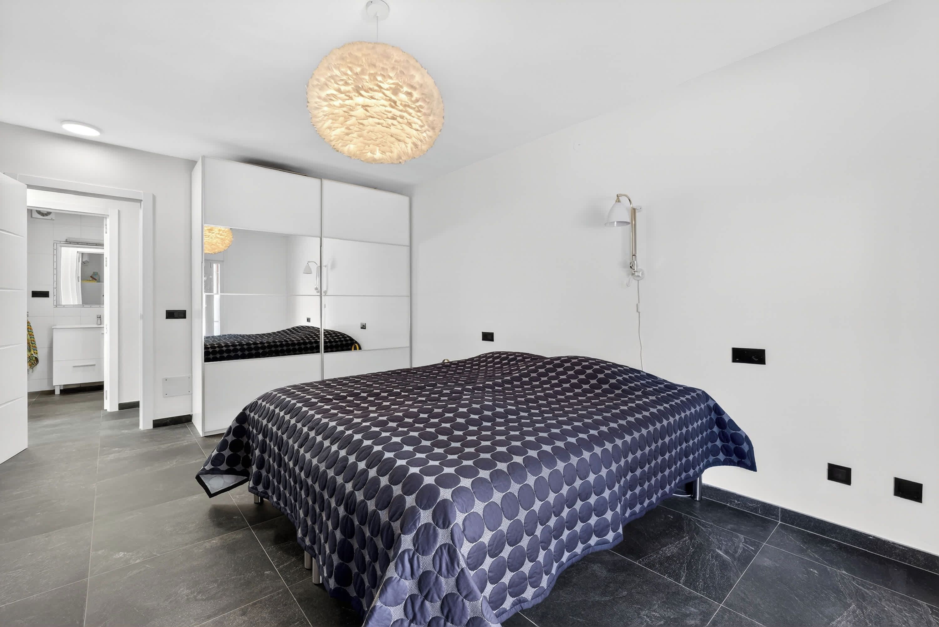 A modern bedroom with a large bed, a hanging light fixture, and a walk-in closet.