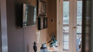 A room with a television mounted on the wall, a glass table with a tray, a potted plant, and a fluffy rug. - Charming cottage on 8 acres of peace & tranquility just a short drive from town. (Boaz)