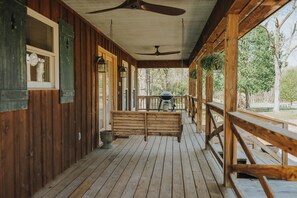 A wooden porch with a ceiling fan, a bench, and a grill area.
