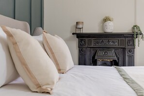 A bedroom with a bed, pillows, a fireplace, and a small table with a lamp. - Stockbridge ‘Little Gem’ Flat, Sleeps 3 (Stockbridge)