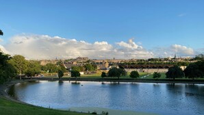 Une rivière traversée par un pont, un parc avec des arbres et, au loin, une vue sur la ville avec ses bâtiments historiques.