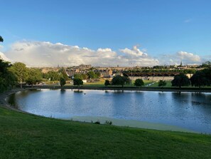 Ein Fluss mit einer Brücke, ein Park mit Bäumen und eine ferne Stadtansicht mit historischen Gebäuden.