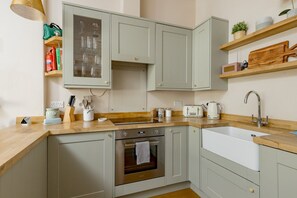 Een keuken met een houten aanrechtblad, roestvrijstalen apparatuur en lichte kastjes.