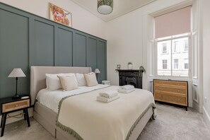 A neatly arranged bedroom with a bed, bedside tables, a fireplace, and a window. - Stockbridge ‘Little Gem’ Flat, Sleeps 3 (Stockbridge)