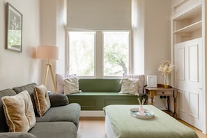 A room with a green bench, a grey sofa, a lamp, and a small table with a vase. - Stockbridge ‘Little Gem’ Flat, Sleeps 3 (Stockbridge)