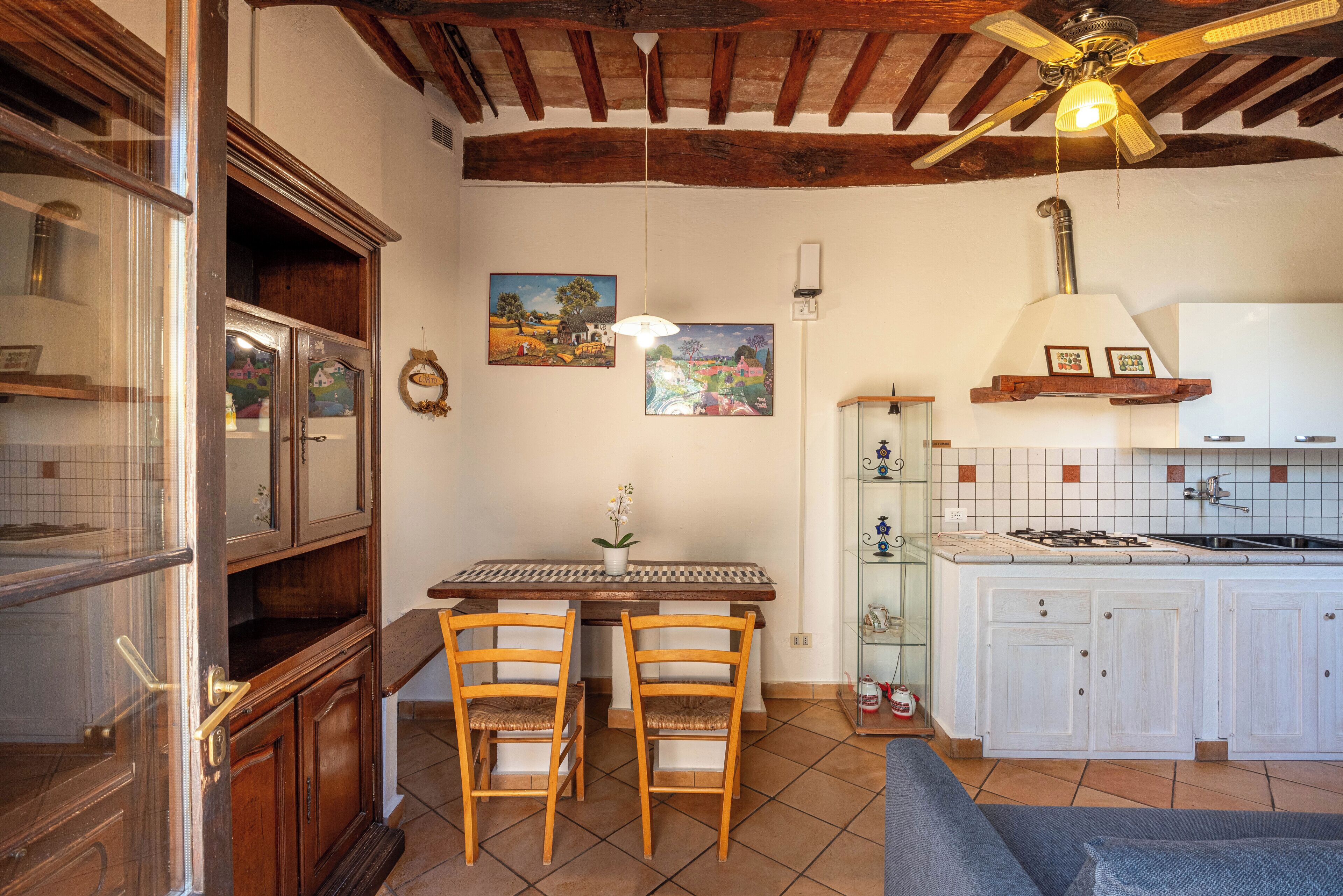 Een keuken met een houten tafel, twee stoelen, een plafondventilator en een betegelde spatwand.