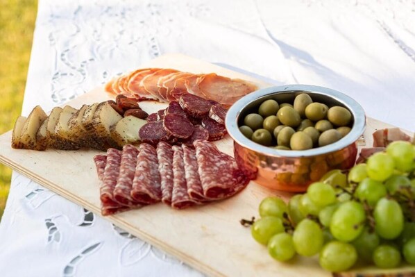 Une planche de charcuterie avec différentes sortes de viandes, des olives et des raisins, le tout disposé sur une planche en bois.