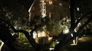 Un edificio de piedra de noche con ventanas iluminadas y árboles circundantes.