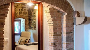 Una habitación con pared de piedra, puerta de madera, una silla y una cama.