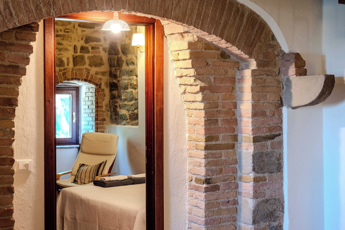 A room with a stone wall, a wooden door, a chair, and a bed.
