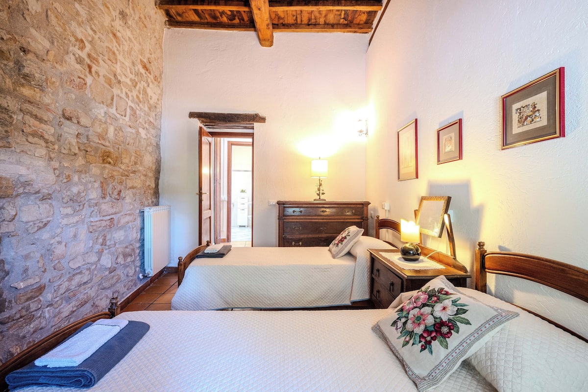 A room with two beds, a wooden headboard, a stone wall, a wooden dresser, and a mirror.