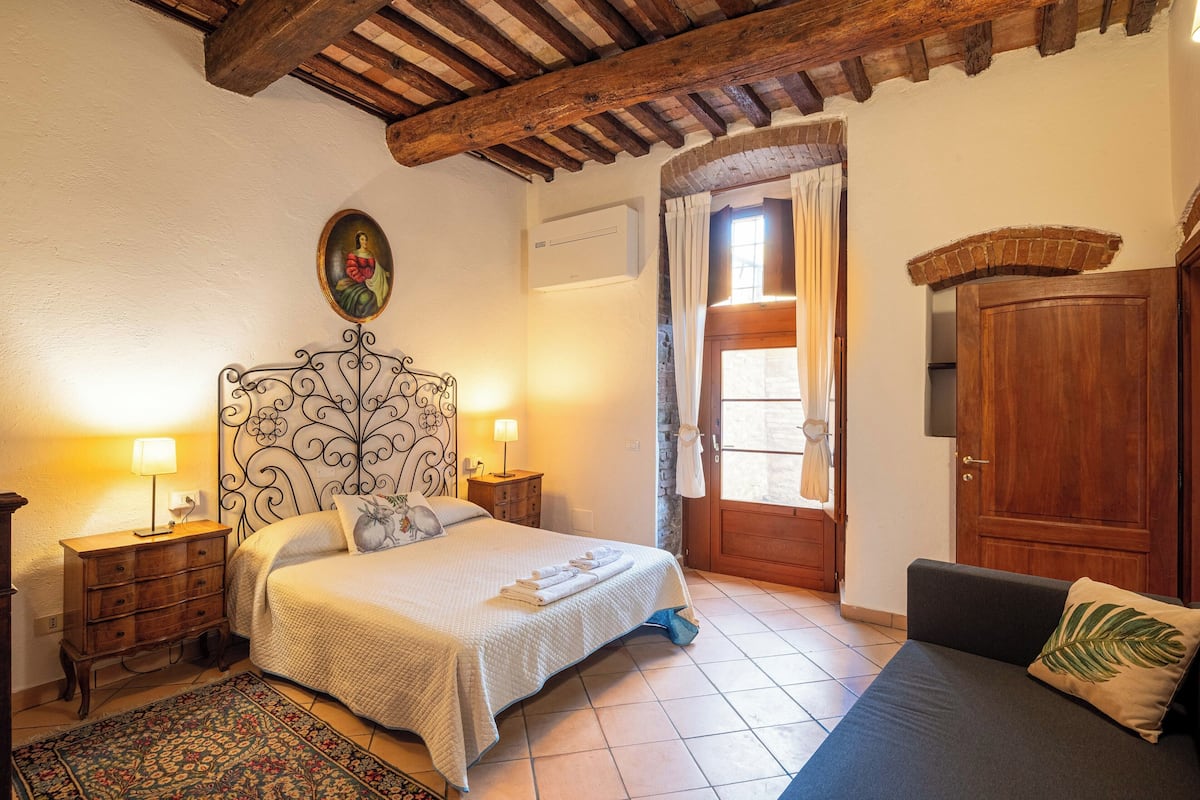 A bedroom with a bed, bedside tables, a wooden door, and a view of the outside.
