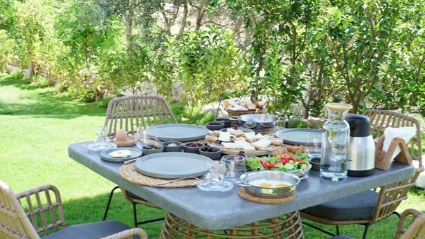 An outdoor dining table set with plates, bowls, and glasses, surrounded by wicker chairs. - Muyo House (Urla)