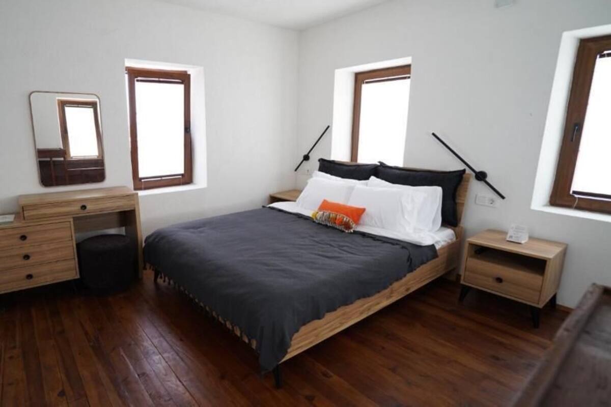 Quarto com uma cama de madeira, penteadeira, espelho, duas mesas de cabeceira e uma janela.