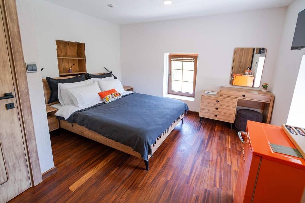 Quarto com cama de madeira, escrivaninha, cadeira, guarda-roupa e janela.