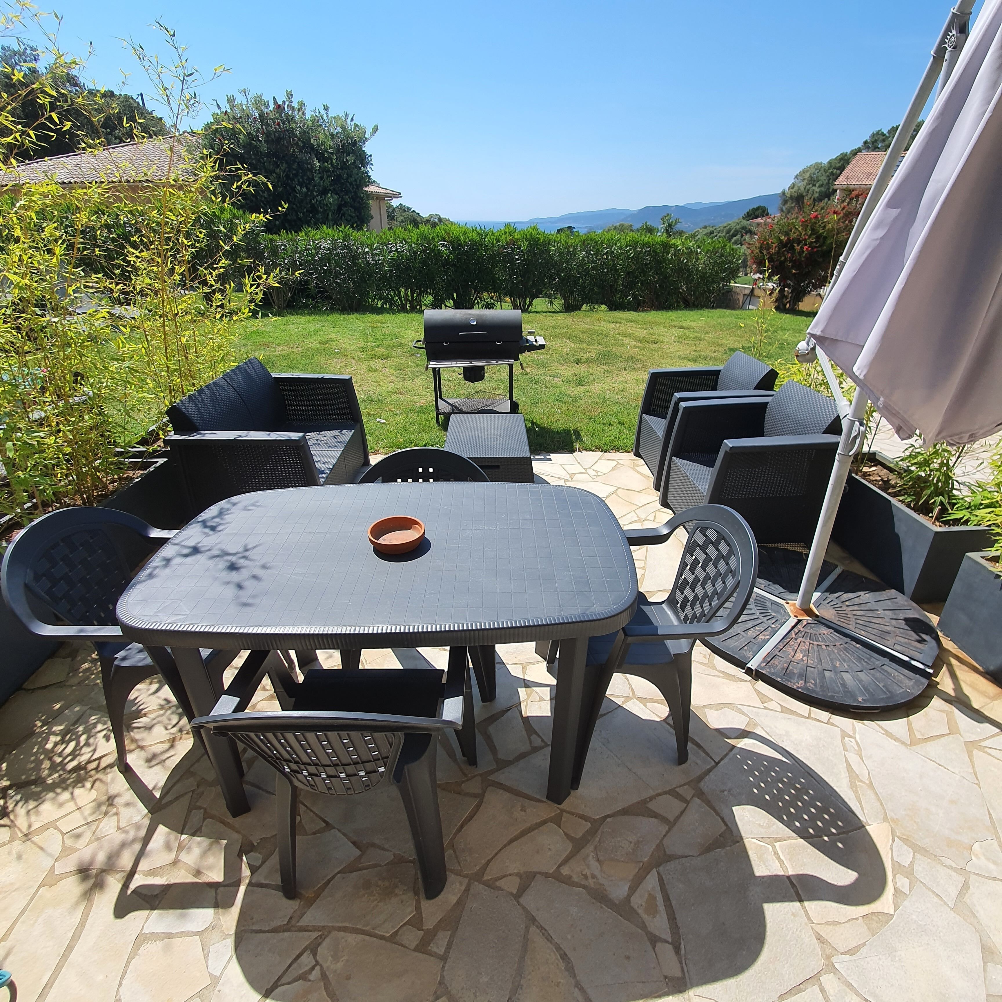 A patio with a table and chairs, a grill, and a view of the landscape.