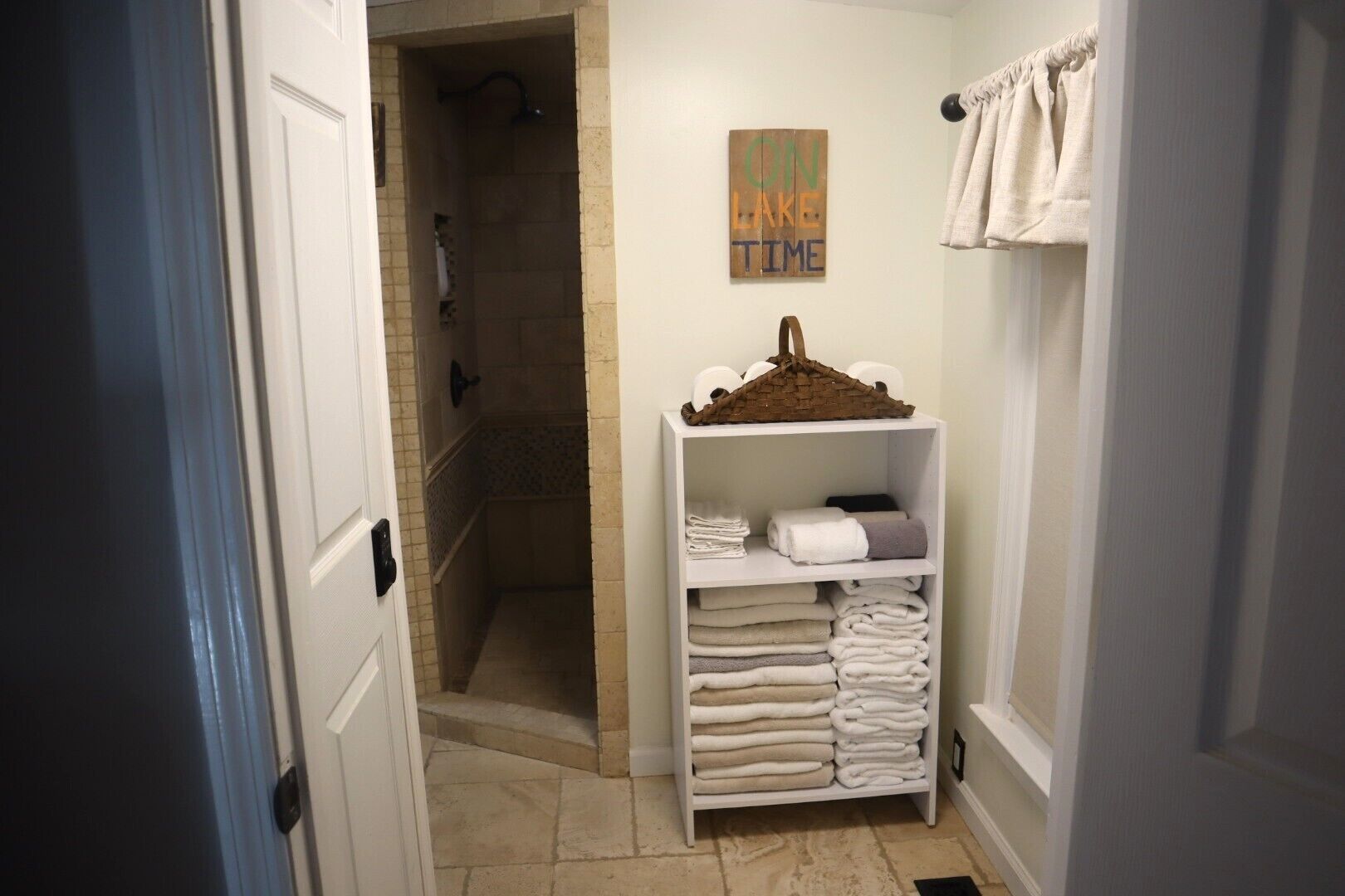 A bathroom with a shower, a shelf with folded towels, and a wall sign.