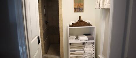 A bathroom with a shower, a shelf with folded towels, and a wall sign.