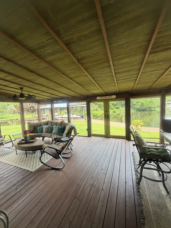 A covered outdoor seating area with a wooden deck, a sofa, chairs, and a table.