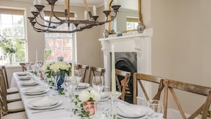 A dining room with a long table set for a meal, a chandelier, and a fireplace.