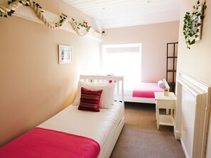 A bedroom with two beds, a small table, a radiator, and a window.