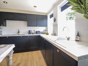A modern kitchen with dark cabinets, white countertops, and a wooden dining table. - The Admiral's Home (Whitehaven)