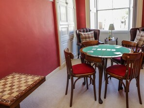 A room with a round table, chairs, a chessboard, and a window with a view.