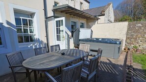 A patio with a round wooden table and chairs, a hot tub, and a stone wall.
