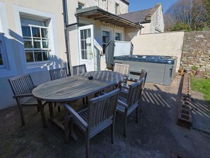 A patio with a round wooden table and chairs, a hot tub, and a stone wall. - The Admiral's Home (Whitehaven)