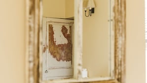 A mirror reflecting a door with peeling paint and a wall-mounted light fixture.