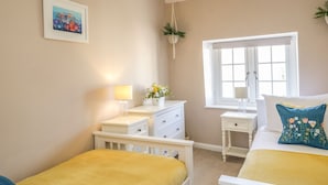 A bedroom with two beds, a window, a bedside table with a lamp, a dresser, and a framed picture on the wall.